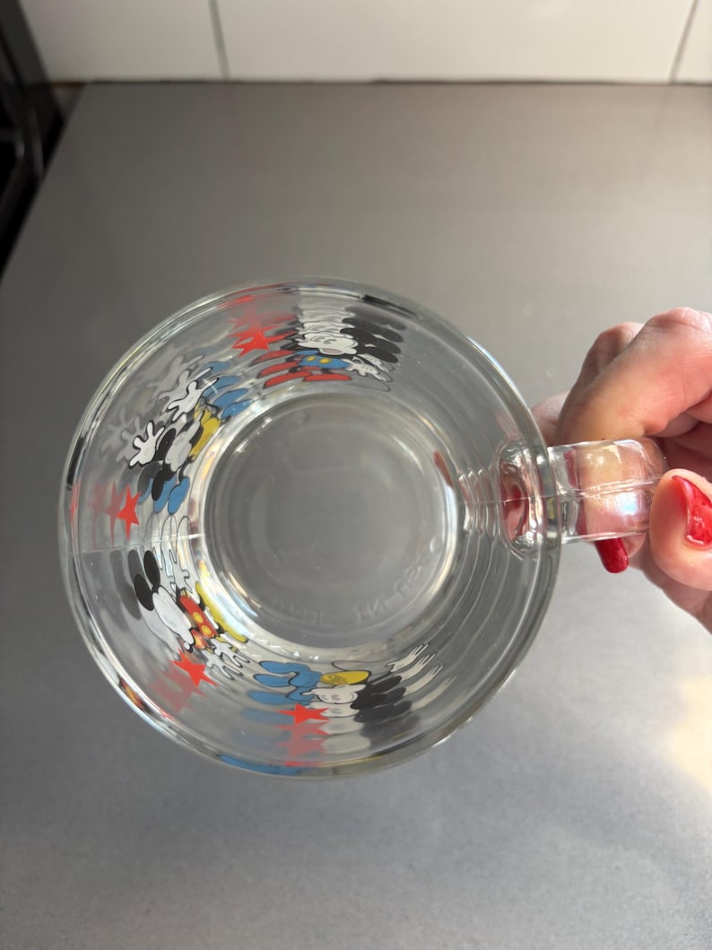 May include: A clear glass mug with a Mickey Mouse design. The mug features red stars and images of Mickey Mouse, Donald Duck, and Goofy.