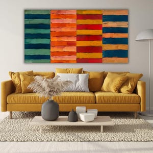 Op de afbeelding: Abstracte kunstcanvas met vier panelen van horizontale penseelstreken in tinten van blauwgroen, oranje, rood en marineblauw. Een mosterdgele bank met kussens staat onder het kunstwerk, met een neutraal tapijt en een salontafel.