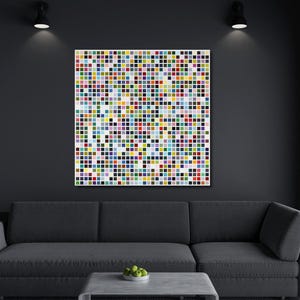 Könnte beinhalten: Ein quadratisches Wandbild mit einem Raster aus zahlreichen kleinen, bunten Quadraten in verschiedenen Rot-, Blau-, Grün-, Gelb-, Lila- und Weißtönen. Das Kunstwerk ist an einer dunkelgrauen Wand über einem dunkelgrauen Sofa und einem Tisch angebracht.