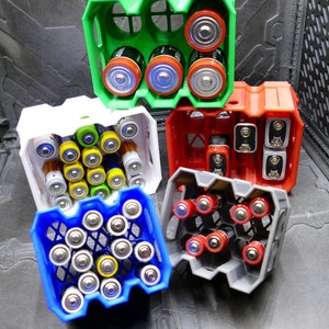 Könnte beinhalten: Fünf Batteriekästen in verschiedenen Farben, darunter grün, weiß, rot, grau und blau. Die Kästen sind mit verschiedenen Batterietypen gefüllt.