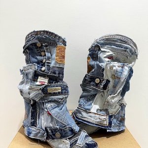 May include: A pair of unique, patchwork denim boots. The boots are constructed from various pieces of blue jeans, featuring button closures, pockets, and Levi's brand tags. The boots are placed on a brown cardboard box.