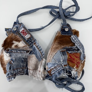 Puede incluir: Top de bikini de mezclilla con parches y detalles de piel de vaca marrón. El top está hecho de vaqueros de mezclilla reciclados, con bolsillos, costuras y la etiqueta "501". Las correas son de tiras de mezclilla, y el diseño es de estilo patchwork.