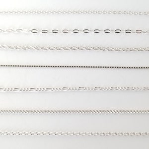 May include: Seven different silver chains of varying styles and thicknesses. The chains are arranged horizontally on a white background.
