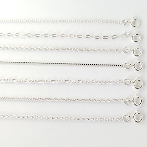 May include: An assortment of silver necklaces showcasing different chain designs, such as cable, oval link, rope, box, figaro, and curb chains. Each necklace is presented on a white backdrop and has a spring ring clasp.