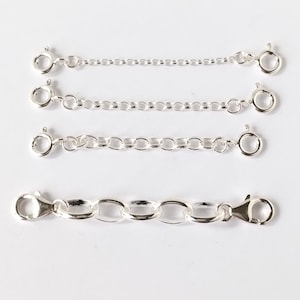 May include: Four silver chain extenders with varying chain link designs. Each extender features a clasp at both ends. These extenders are used to lengthen necklaces or bracelets. The background is white.