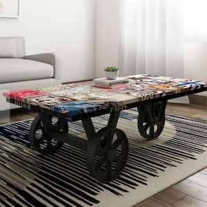 May include: A black metal coffee table with four wheels. The table top is made of wood and has a patchwork design with images of Paris, London, and other cities. The table is sitting on a black and white striped rug.