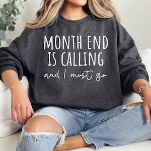 Può includere: Una felpa grigia scura con il testo "Month End Is Calling and I Must Go" in lettere bianche.