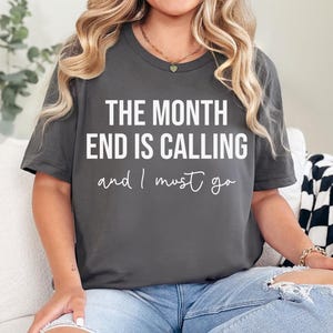 Può includere: Una maglietta grigia scura con testo bianco che recita "The month end is calling and I must go."