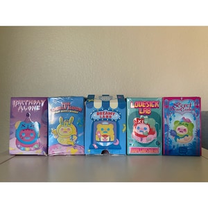May include: Five colorful boxes with cartoon characters on them. The boxes are labeled "Birthday Alone", "The Lonely Moon", "Dreamy Land", "Lovesick Lab", and "The Secret Bear Garden".