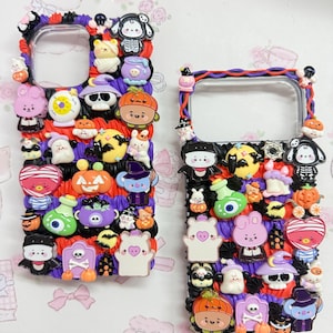 May include: Two rectangular phone cases decorated with textured purple and orange piping. The cases feature various miniature Halloween-themed charms including pumpkins, ghosts, skulls, bats, potions, and cartoon characters in vibrant colors.