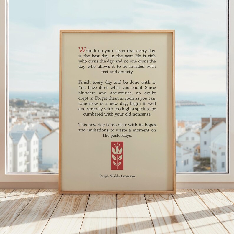 May include: A beige framed print with a quote by Ralph Waldo Emerson about making the most of each day. The quote is set against a blurry background of a cityscape.