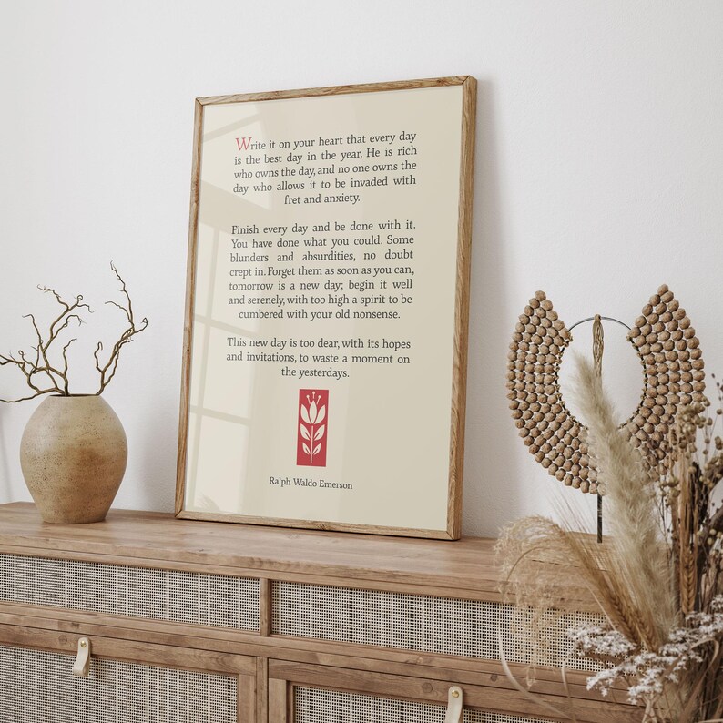 May include: A framed print with a white background and red floral design. The print features a quote by Ralph Waldo Emerson about living in the present moment. "Write it on your heart that every day is the best day in the year. He is rich who owns the day, and no one owns the day who allows it to be invaded with fret and anxiety. Finish every day and be done with it. You have done what you could. Some blunders and absurdities, no doubt crept in. Forget them as soon as you can, tomorrow is a new day; begin it well and serenely, with too high a spirit to be cumbered with your old nonsense. This new day is too dear, with its hopes and invitations, to waste a moment on the yesterdays. - Ralph Waldo Emerson"