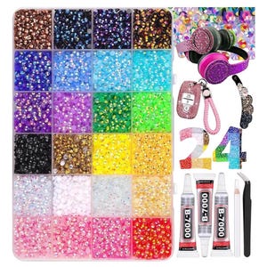 Puede incluir: Una colección de pedrería de colores en un recipiente dividido, junto con auriculares con adornos, un llavero de coche, una pinza para el pelo, los números 24, tubos de pegamento y pinzas. La pedrería es de varios colores.