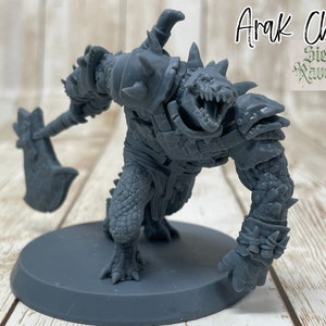 May include: A gray plastic miniature of an Arak Chief from the Siege of Ravenhold board game. The miniature is holding a large axe and is wearing armor.