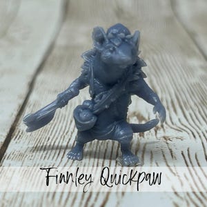 May include: A gray figurine of a mouse-like character, "Finnley Quickpaw", stands with a weapon and a satchel. The figure is detailed with armor and a tail, set against a wood-grain background.