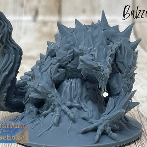 May include: Gray 3D printed miniature of a monstrous creature with a spiky, reptilian body and a long, flowing tail. The creature is crouched on a round base, with its mouth open in a menacing snarl. The miniature is labeled "Baltzur".