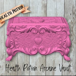 May include: A bright pink rectangular chest featuring intricate relief carvings of scrolling foliage and a central heart motif. A tan banner with the text Health Potion is positioned above the chest, and the text Health Potion Arcane Vault is below.