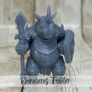May include: A gray rhinoceros figurine in a warrior pose, holding a spear and shield. The figurine is wearing armor and has a prominent horn. The text "Rhinoceros Fighter" is written at the bottom.