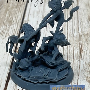 May include: A group of four gray painted miniature figurines of imps or devils, with wings and horns, are piled on top of each other. They are standing on a pile of books, with the text "Bestiarium of the Mad Scholar" visible on the base. The text "MonklingS" is visible in the top left corner of the image.