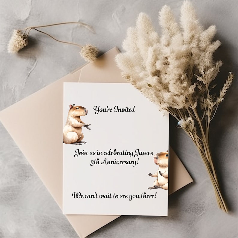 May include: A white card with a black border and text that reads "You're Invited" and "Join us in celebrating James 5th Anniversary! We can't wait to see you there!"  Two cartoon capybaras are on the card, one on each side of the text.