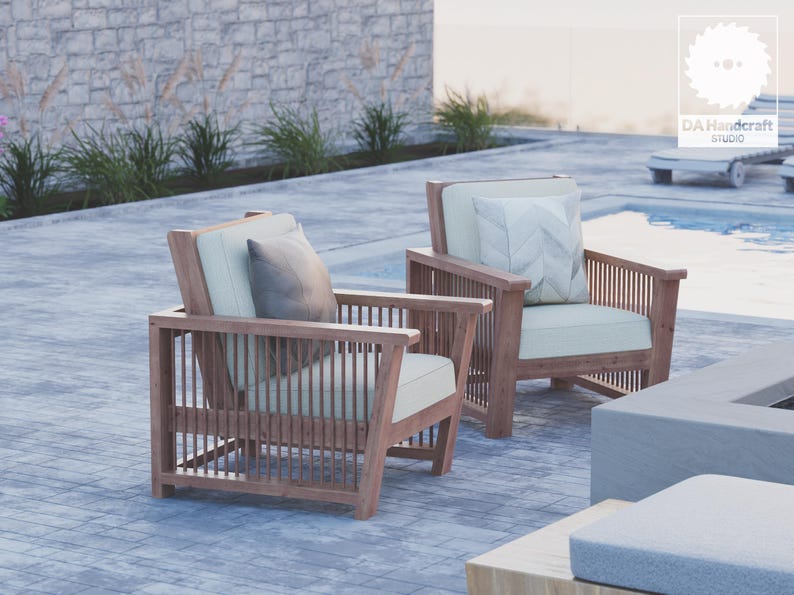 May include: Two wooden chairs with light beige cushions and a brown pillow on each chair. The chairs are positioned on a gray concrete patio near a swimming pool.