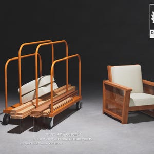 May include: A metal cart loaded with wooden dowels, fence pickets, and cedar tone wood studs. The cart has a metal frame and wheels. A wooden chair with a white cushion sits in the background.