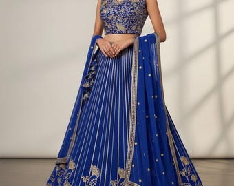 Può includere: Un abito formale blu reale con ricami floreali dorati. Il top senza maniche e la gonna ampia sono adornati da intricati motivi dorati. Una sciarpa trasparente abbinata è drappeggiata sulle spalle. L'abito è adatto per occasioni speciali.