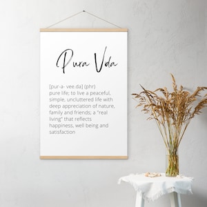 Könnte beinhalten: Ein weißer Poster mit einem Holzrahmen, der den Satz "Pura Vida" in schwarzer Kursivschrift zeigt. Der Poster definiert "Pura Vida" als einen spanischen Ausdruck, der "reines Leben" bedeutet und es als eine friedliche, einfache und aufgeräumte Lebensweise beschreibt.