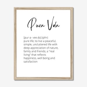 May include: A framed print with a white background and black text. The text reads "Pura Vida" in a stylized font, followed by a definition of the phrase in brackets: [pur-a- vee.da] (phr) pure life; to live a peaceful, simple, uncluttered life with deep appreciation of nature, family and friends; a "real living" that reflects happiness, well being and satisfaction.