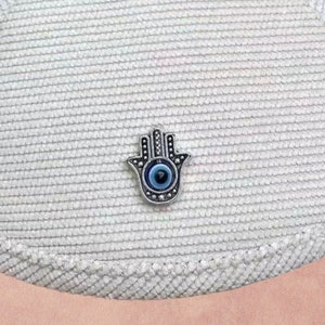 May include: A silver charm in the shape of a hand with a blue evil eye in the center.
