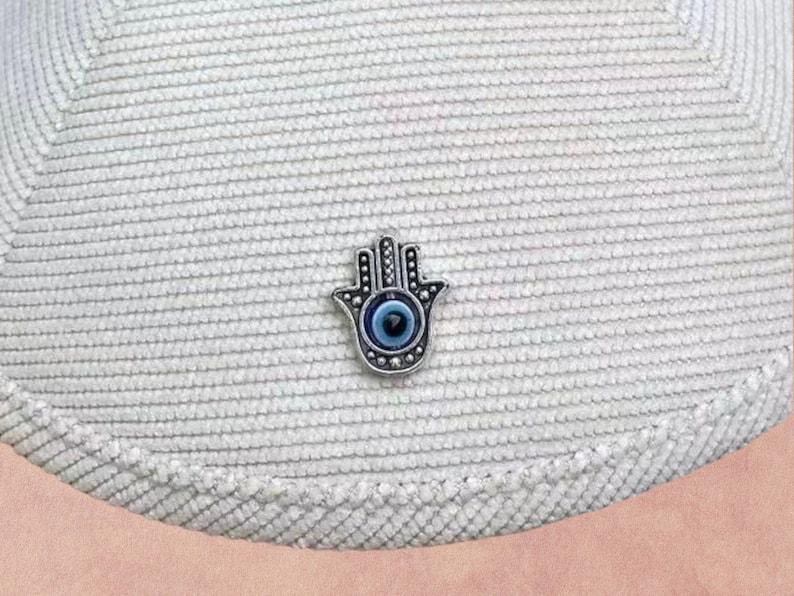 May include: A silver charm in the shape of a hand with a blue evil eye in the center.
