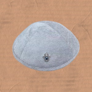 May include: A gray knitted kippah with a silver Hamsa hand charm with a blue eye in the center.