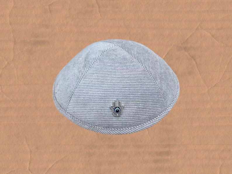 May include: A gray knitted kippah with a silver Hamsa hand charm with a blue eye in the center.