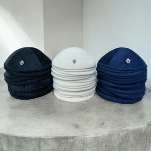 May include: Three kippahs, one black, one white, and one navy blue, each with a small silver charm on top.