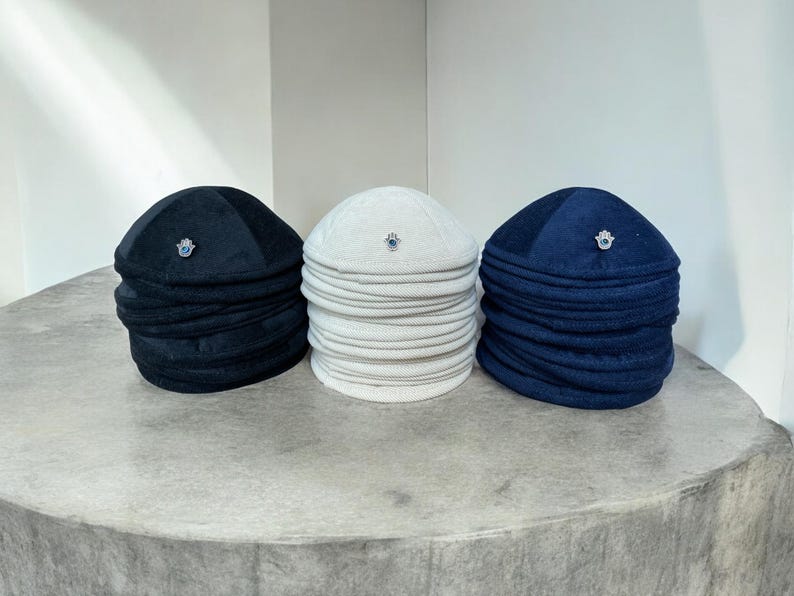May include: Three kippahs, one black, one white, and one navy blue, each with a small silver charm on top.
