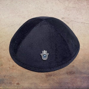 May include: A black velvet kippah with a silver Hamsa hand charm featuring a blue evil eye.