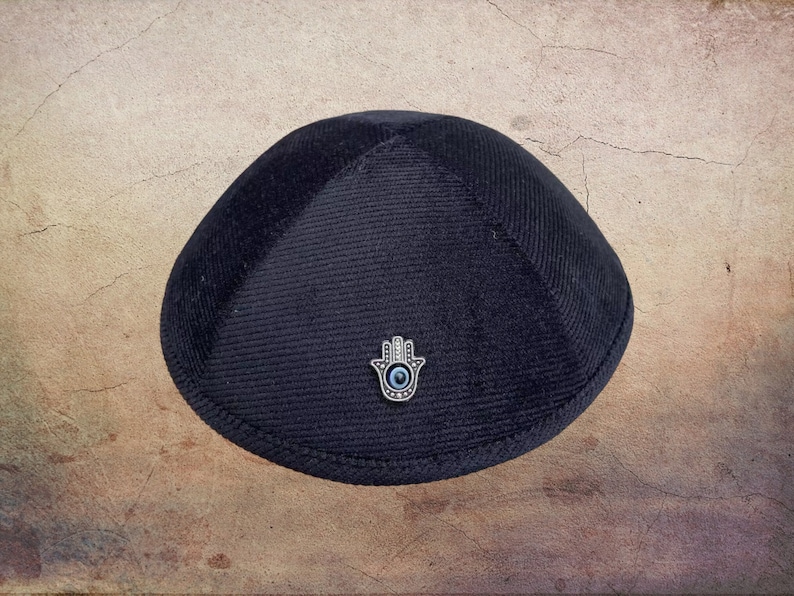 May include: A black velvet kippah with a silver Hamsa hand charm featuring a blue evil eye.