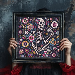 May include: A black framed print featuring a colourful floral design with a skeleton and skull. The skeleton is surrounded by flowers in shades of pink, yellow, blue and green.
