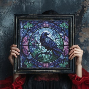 Könnte beinhalten: Ein gerahmtes Buntglasfenster mit einem schwarzen Raben in der Mitte. Der Rabe sitzt auf einem Ast, umgeben von rosa und blauen Blumen. Der Rahmen ist schwarz und das Glas ist eine Mischung aus Blau, Grün und Rosa.