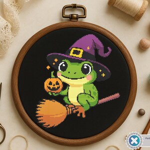 May include: A cross-stitch embroidery of a green frog wearing a purple witch hat and holding a jack-o'-lantern. The frog is riding a broom against a black background, framed in a wooden hoop. Halloween-themed craft.