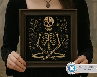 Puede incluir: Obra de arte de punto de cruz enmarcada, que representa un esqueleto dorado en una postura de yoga sobre un fondo negro con elementos florales. La imagen está marcada con una insignia "Pattern Keeper TESTED". Una pieza única.
