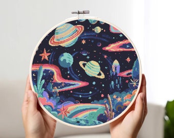 Op de afbeelding: Een kleurrijke borduurring met een ruimtethema. Het ontwerp bevat planeten, sterren en regenbogen op een donkerblauwe achtergrond.