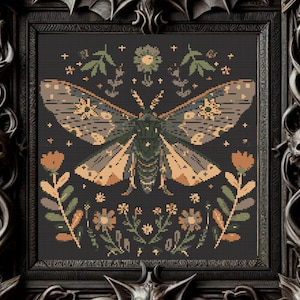 Op de afbeelding: Een borduurwerk met kruissteek van een nachtvlinder met ingewikkelde details, omringd door kleine bloemen in tinten oranje, geel en groen op een zwarte achtergrond.