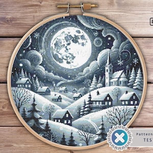 Könnte beinhalten: Ein Kreuzstichmuster, das eine Winterszene mit einem großen Vollmond am Himmel zeigt. Das Dorf liegt eingebettet in einer schneebedeckten Landschaft mit Bäumen und Häusern. Das Muster ist in Schwarzweiß.