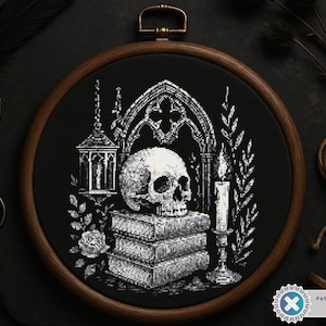 May include: A black and white cross-stitch design of a skull atop stacked books, framed in a wooden embroidery hoop. The gothic scene includes a candle, lantern, and arched window, with additional decorative elements.