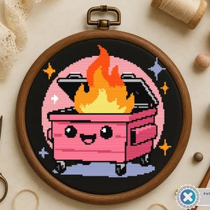 May include: Cross-stitch embroidery in a wooden hoop features a pink dumpster on fire with a smiling face. The design includes a black background, orange flames, and star accents. The hoop is approximately 6 inches in diameter.