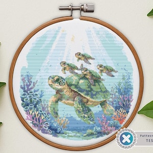 May include: A cross-stitch embroidery of a sea turtle swimming underwater with four smaller turtles on its back. The design is in a wooden hoop, featuring shades of blue, green, and coral. The image is labeled "Pattern Keeper TESTED."