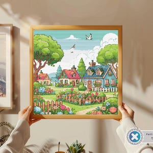 Könnte beinhalten: Ein Kreuzstichmuster, das ein farbenfrohes, fantasievolles Dorf mit Häusern, Bäumen und Blumen zeigt. Die Häuser haben blaue, grüne und rote Dächer. Der Himmel ist blau mit weißen Wolken. Das Muster ist in einem Holzrahmen gerahmt.