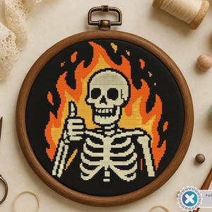 Könnte beinhalten: Kreuzstich-Stickerei in einem Holzrahmen mit einem Skelett, das einen Daumen hochhält, umgeben von Flammen. Das Design verwendet schwarzes, orangefarbenes und cremefarbenes Garn. Der Rahmen wird mit Bastelzubehör wie Scheren und Garnrollen präsentiert.