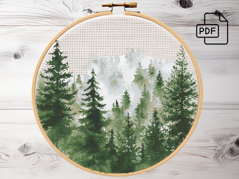May include: Cross stitch pattern of a forest scene with green trees and a white foggy background. The pattern is in a round wooden embroidery hoop.